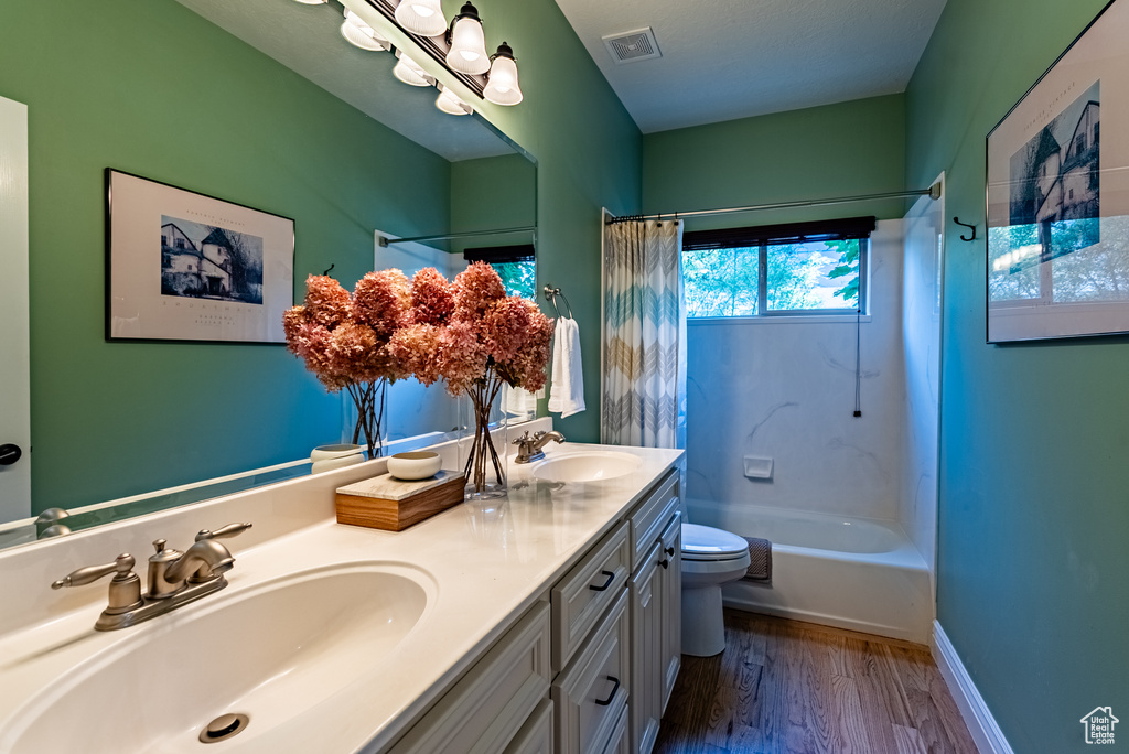 Bathroom with double vanity, wood finished floors, and shower / bath combo with shower curtain