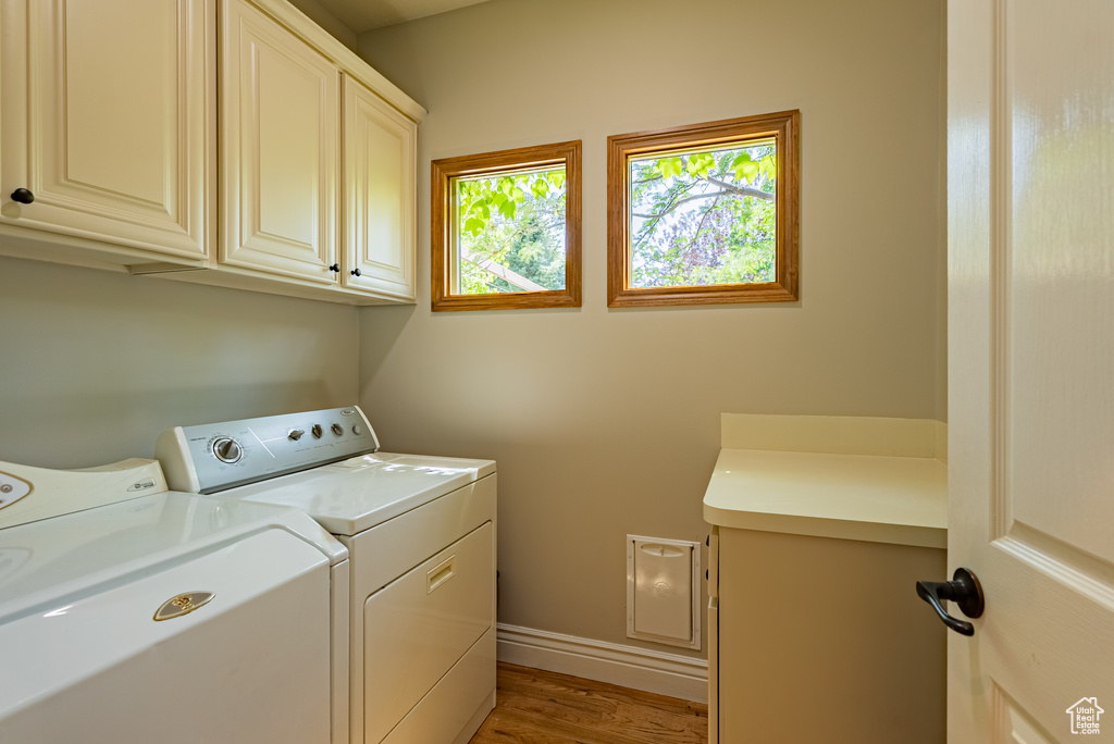 Laundry area with cabinet space, separate washer and dryer, and light wood-type flooring