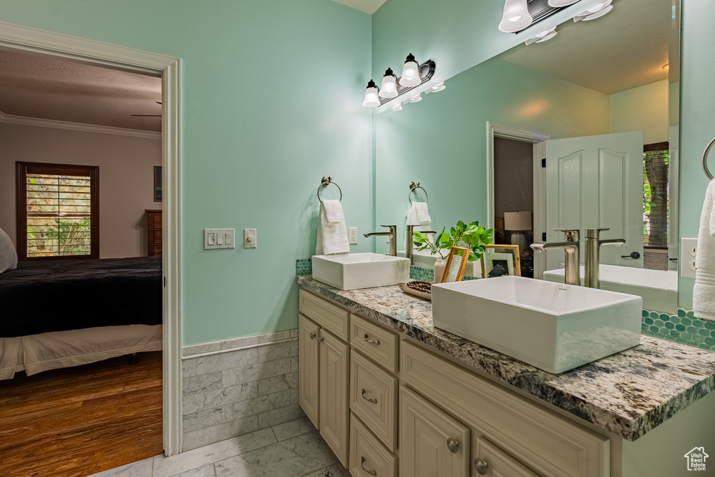Ensuite bathroom with double vanity, ornamental molding, and a wainscoted wall