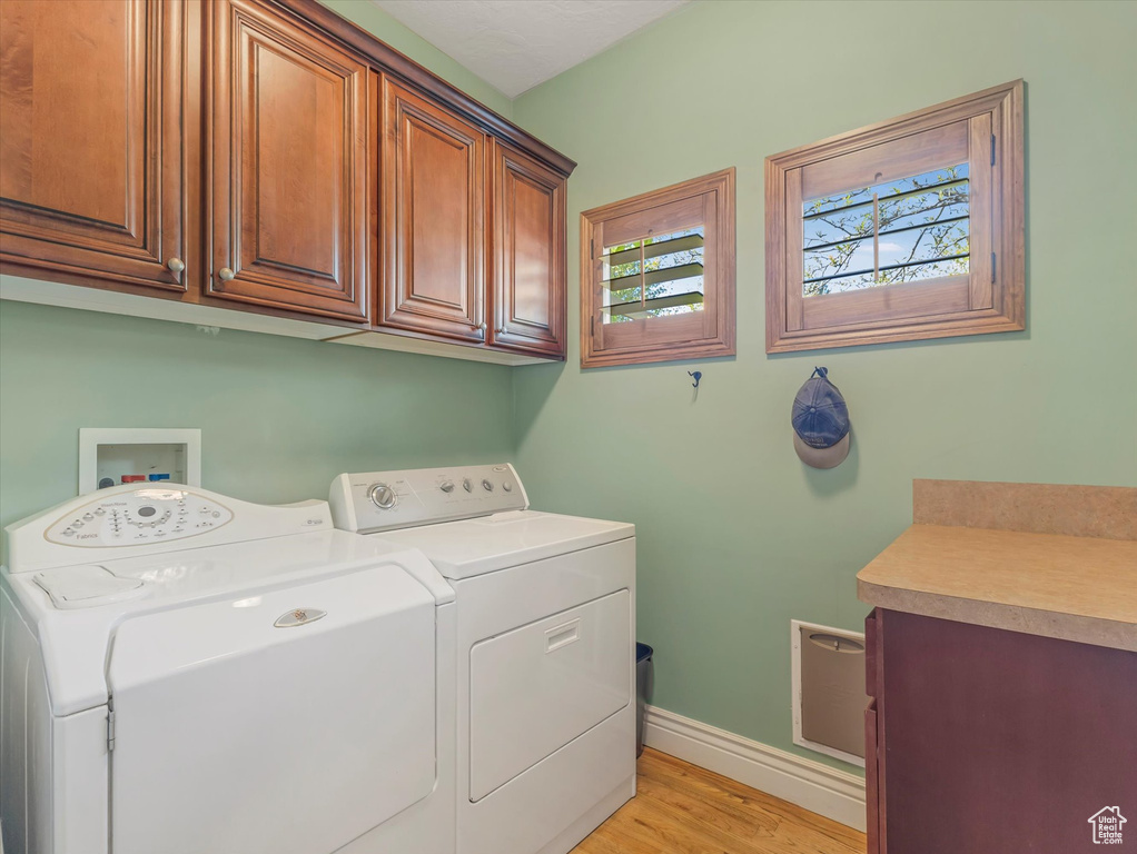 Washroom with baseboards, light wood finished floors, independent washer and dryer, and cabinet space