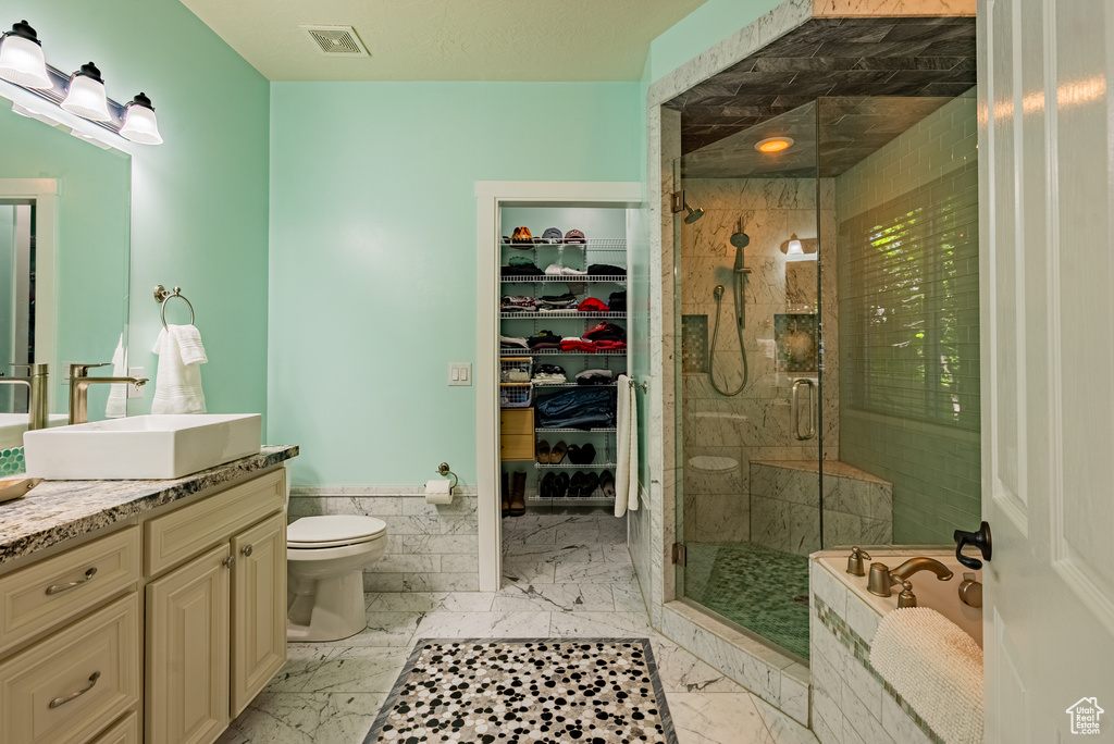 Full bathroom featuring vanity, a shower stall, marble finish flooring, a bath, and wainscoting