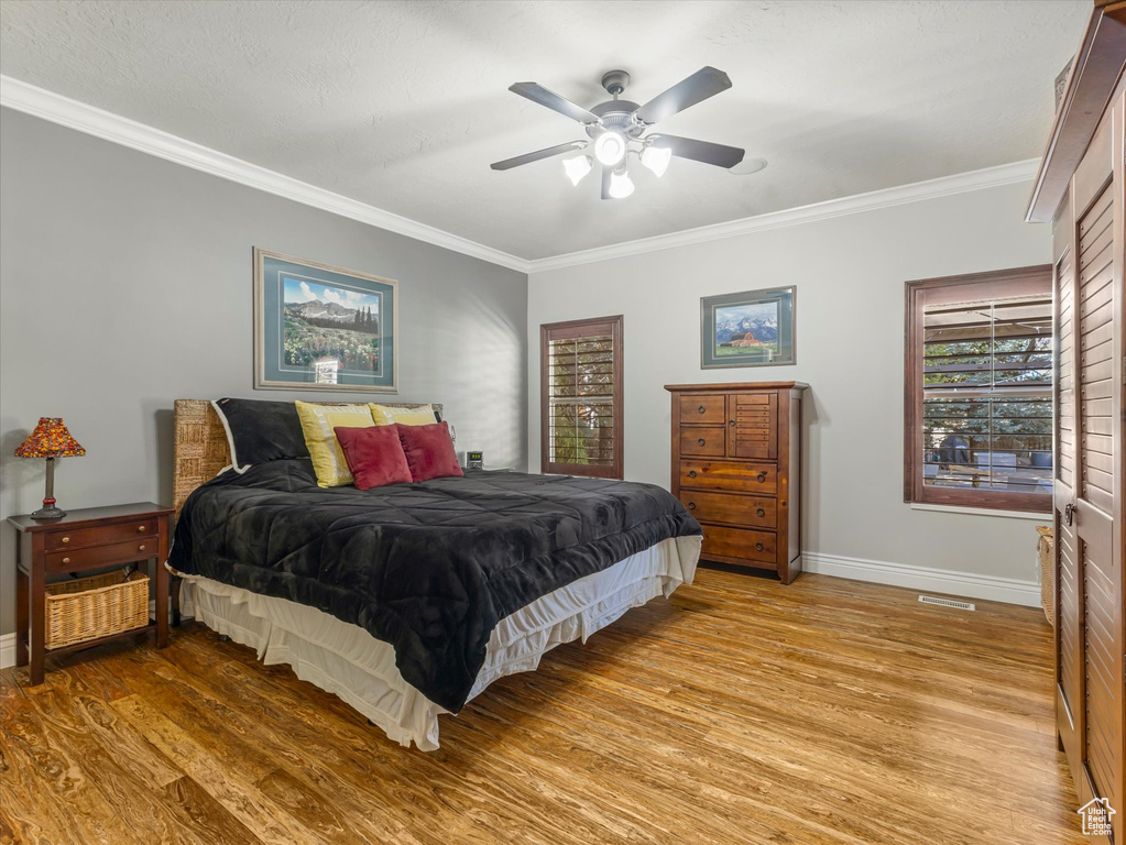 Bedroom featuring light wood-style floors, baseboards, crown molding, and ceiling fan