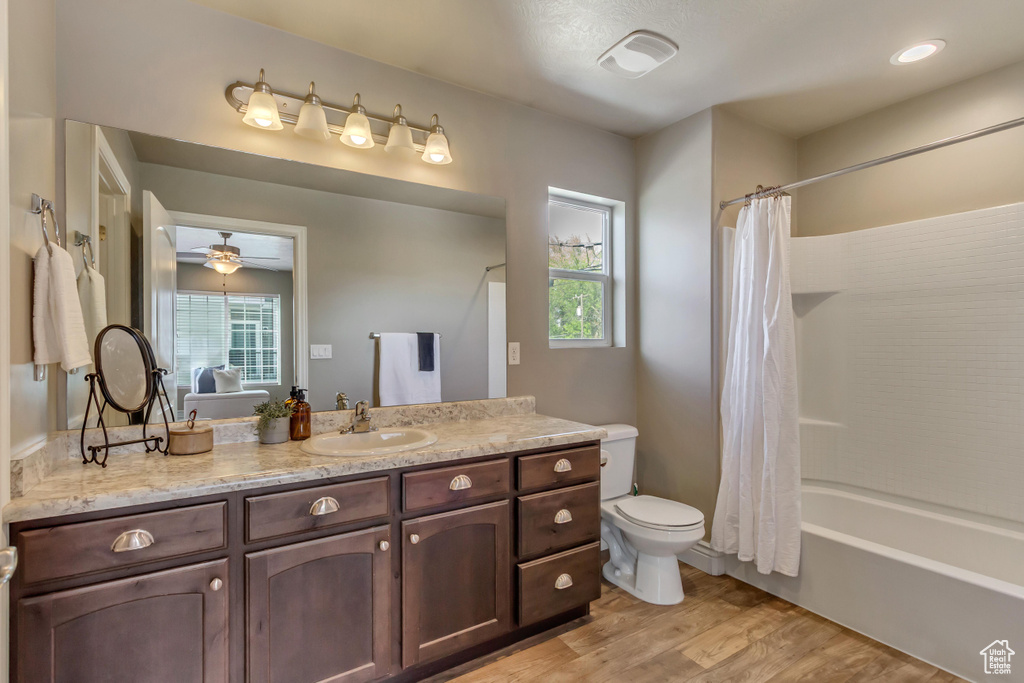 Full bathroom with wood finished floors, shower / bath combination with curtain, ceiling fan, toilet, and vanity