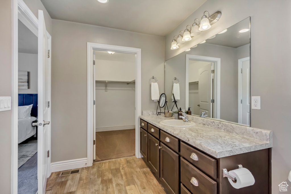 Ensuite bathroom featuring vanity, a walk in closet, visible vents, wood finished floors, and ensuite bathroom