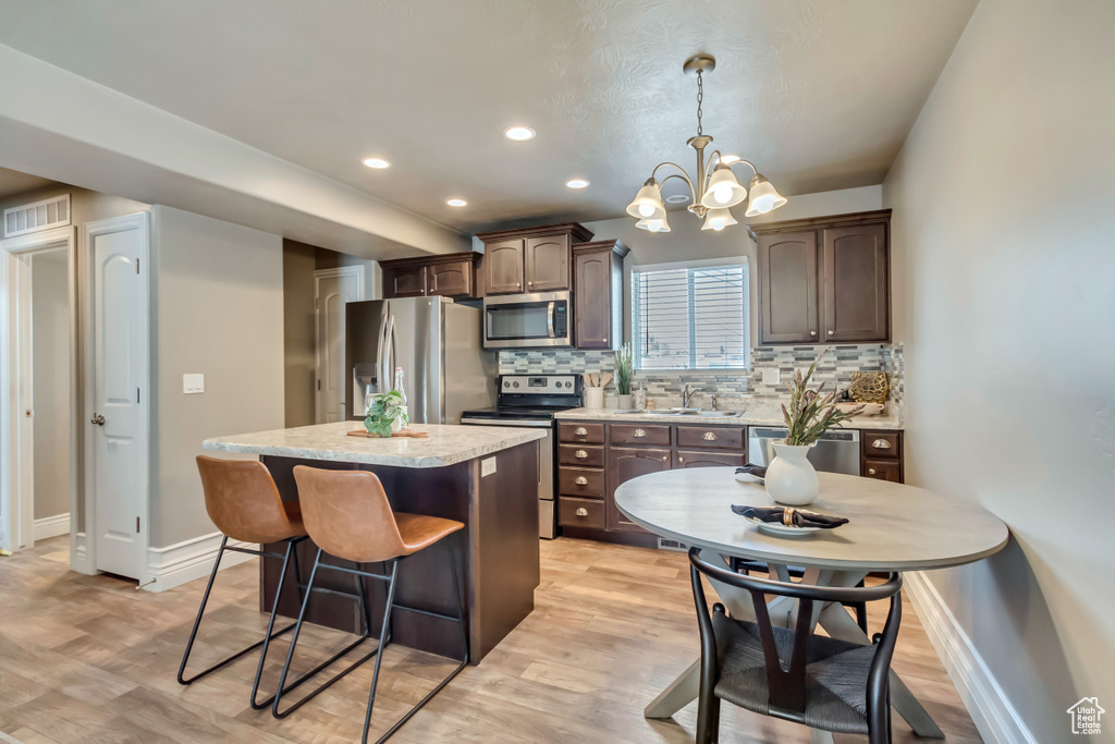 Kitchen featuring appliances with stainless steel finishes, a kitchen island, dark brown cabinets, a sink, and baseboards