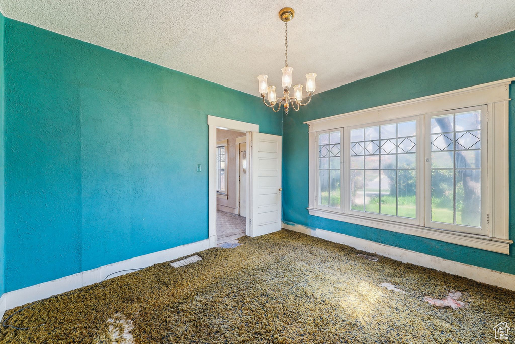 Carpeted empty room with baseboards, a textured ceiling, and a chandelier