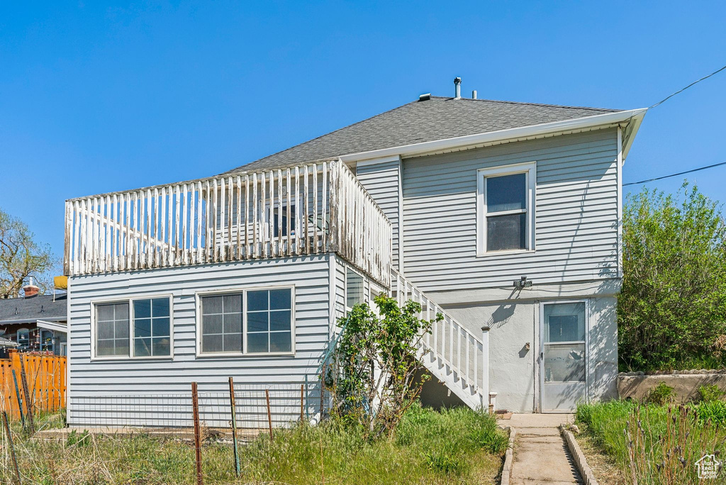 Rear view of property featuring fence, stairs, and roof with shingles