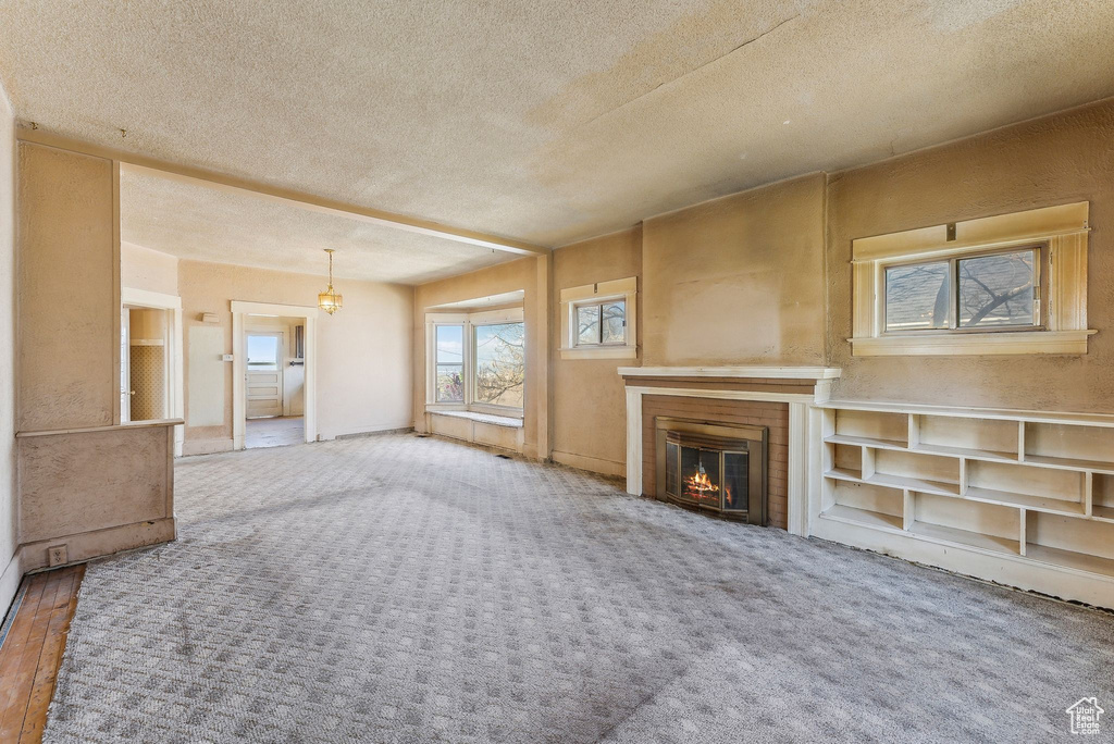 Unfurnished living room with a glass covered fireplace, carpet floors, and a textured ceiling