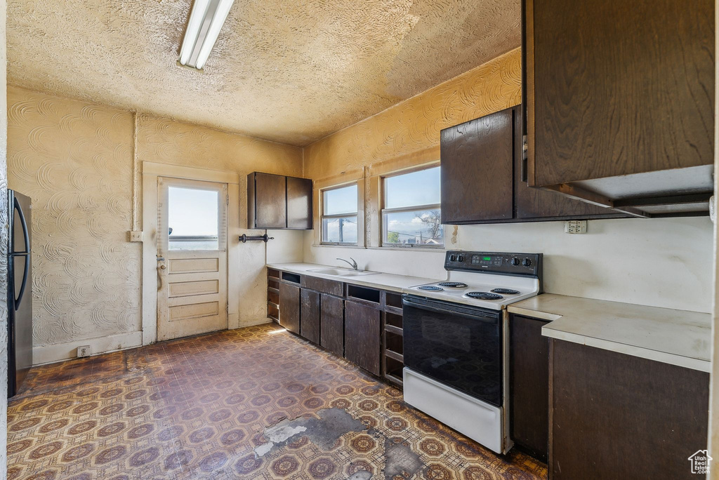Kitchen featuring a sink, light countertops, electric range, and dark brown cabinets