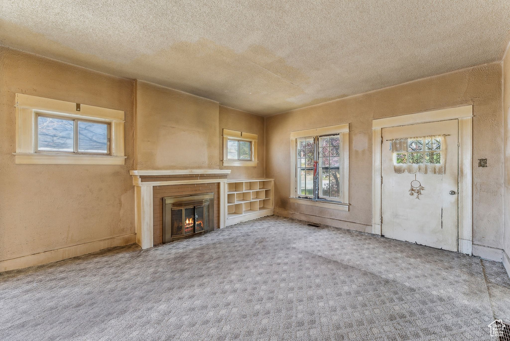 Unfurnished living room featuring carpet flooring, a textured ceiling, and a glass covered fireplace