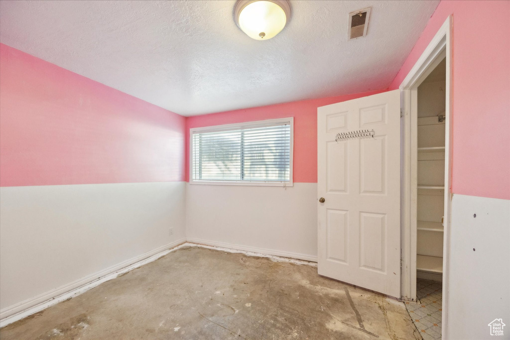 Spare room featuring a textured ceiling, visible vents, concrete floors, and baseboards