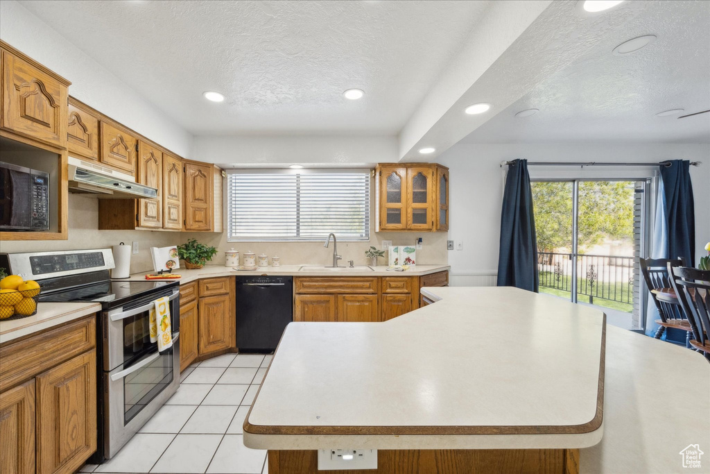 Kitchen with a textured ceiling, under cabinet range hood, black dishwasher, and range with two ovens