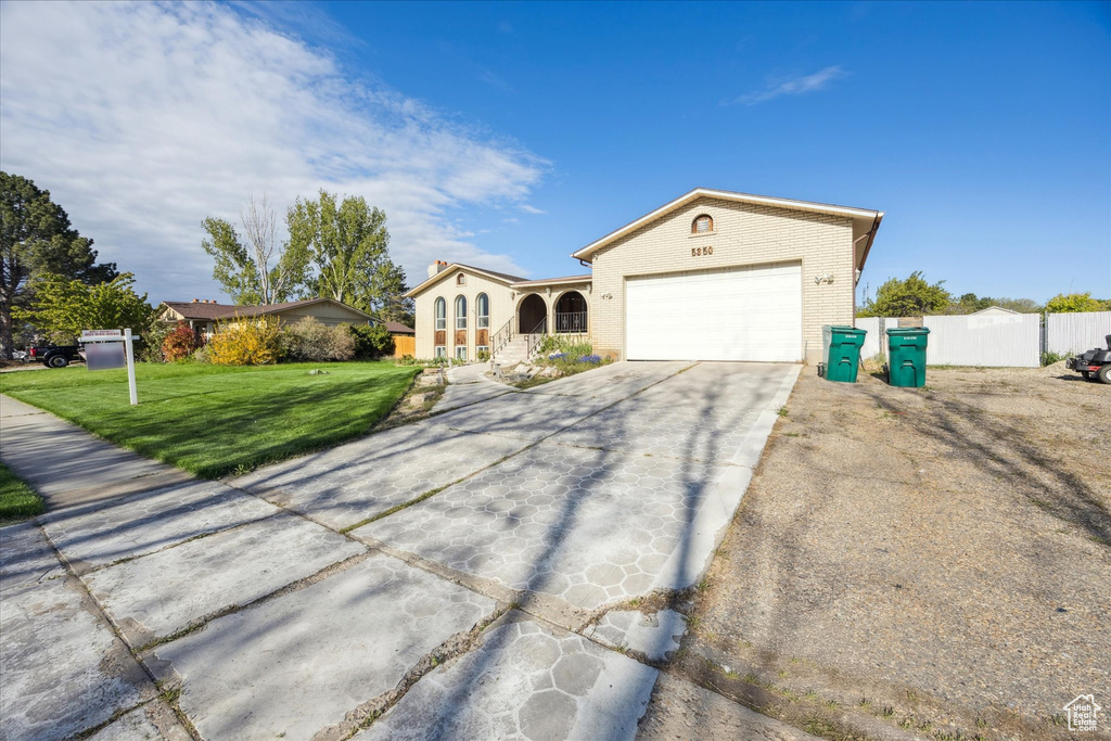 View of front of house with a garage, a front lawn, fence, and concrete driveway