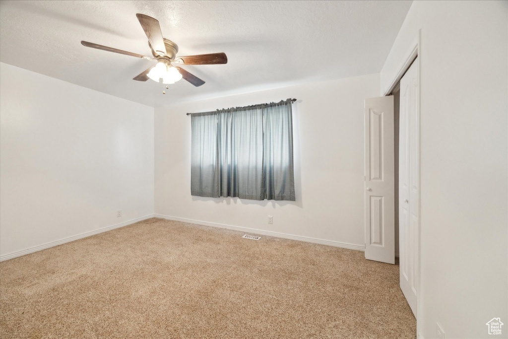 Spare room featuring baseboards, light carpet, a ceiling fan, and visible vents