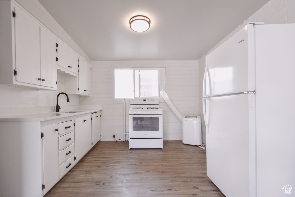 Kitchen featuring a sink, light countertops, white cabinets, light wood finished floors, and white appliances