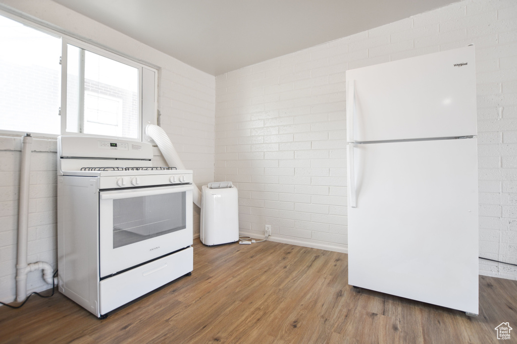 Kitchen with white appliances, concrete block wall, and wood finished floors