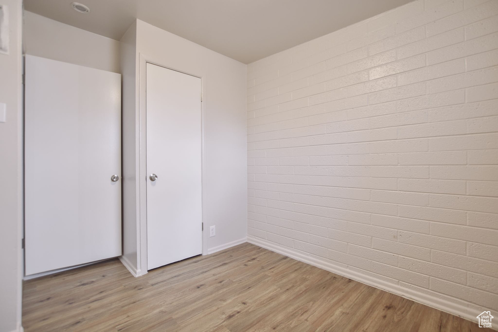 Unfurnished bedroom with light wood-type flooring, baseboards, and brick wall