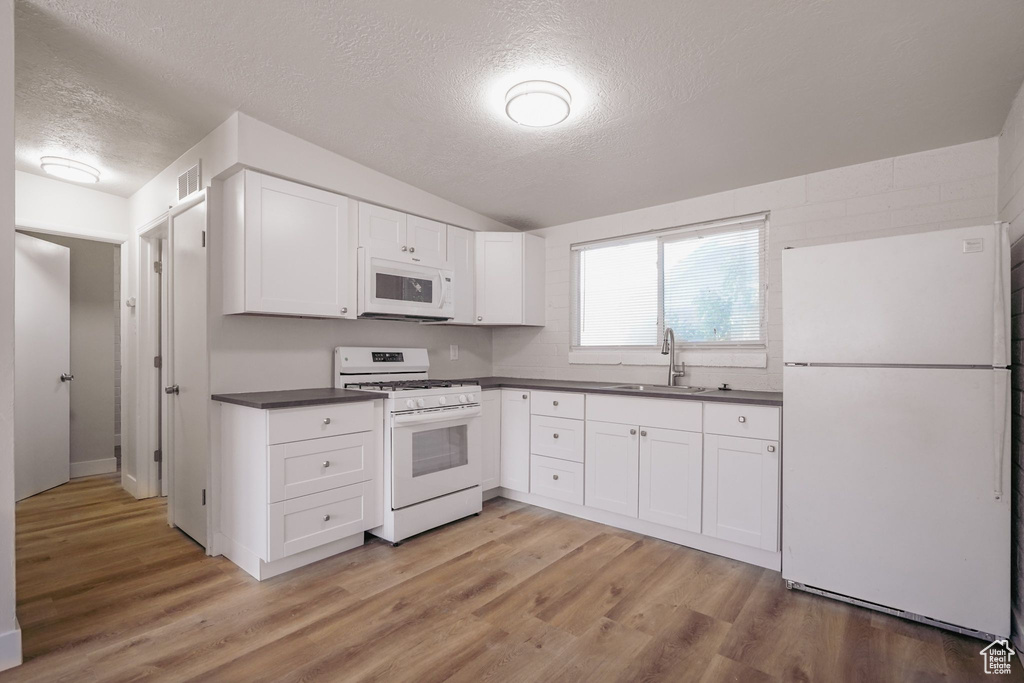 Kitchen with white cabinets, dark countertops, a sink, white appliances, and a textured ceiling