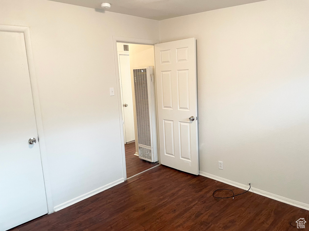 Unfurnished bedroom featuring a heating unit, baseboards, and wood finished floors