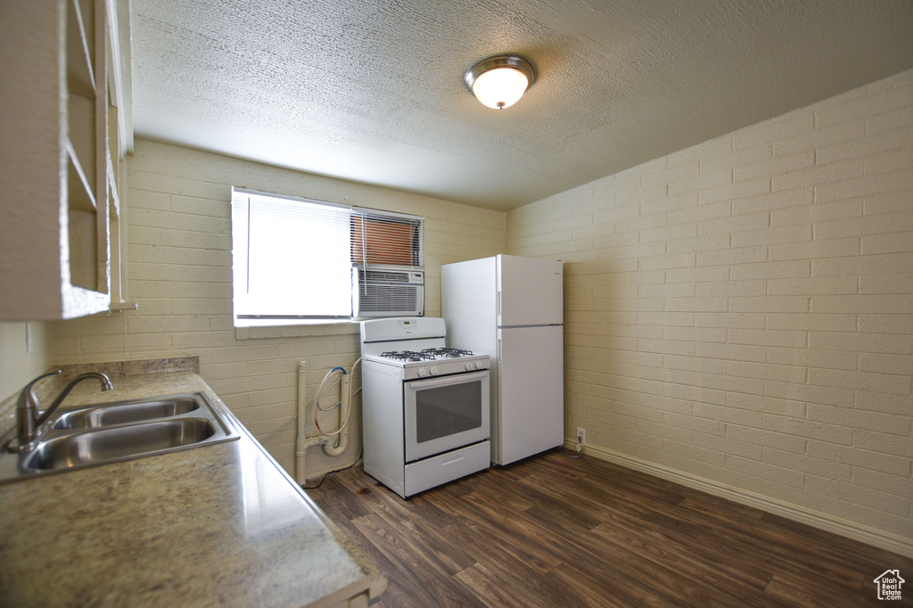 Kitchen featuring dark wood-type flooring, a sink, a textured ceiling, and white appliances