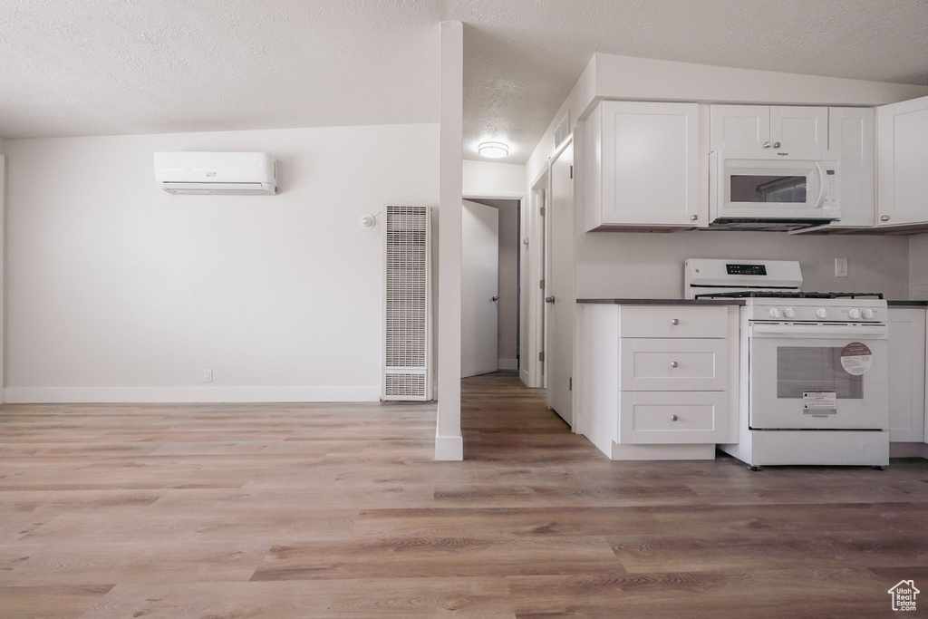 Kitchen with a heating unit, white cabinetry, a wall mounted AC, and white appliances