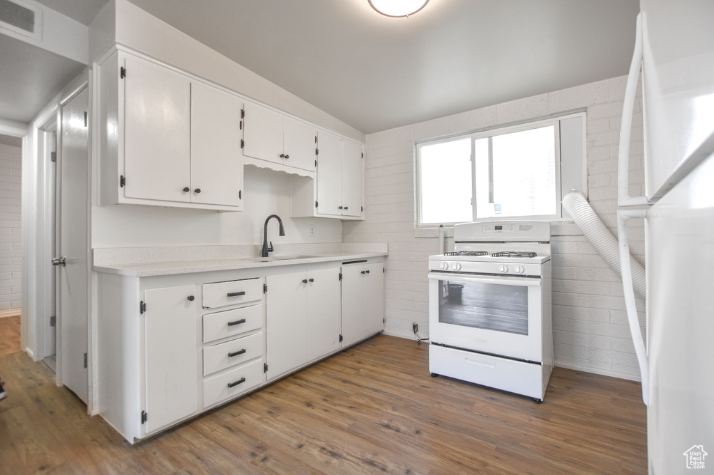 Kitchen featuring visible vents, wood finished floors, white appliances, white cabinets, and a sink