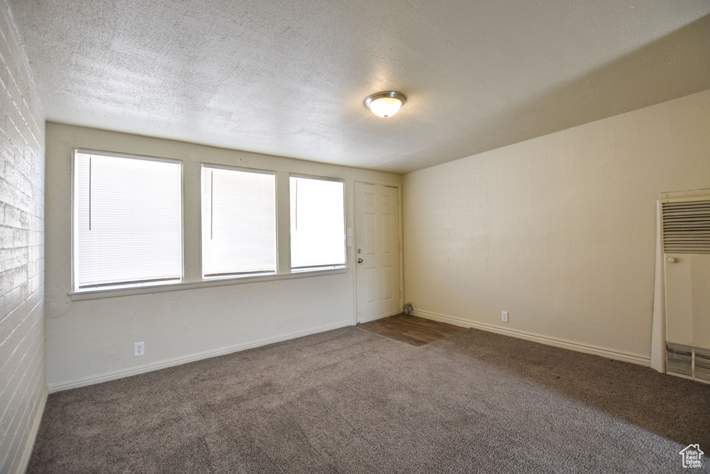 Empty room with baseboards, carpet, a textured ceiling, and a heating unit