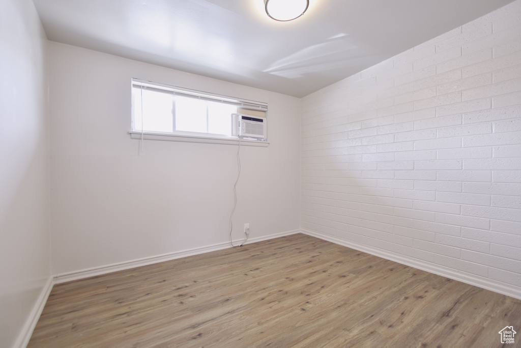 Unfurnished room with baseboards, a wall unit AC, light wood finished floors, and brick wall