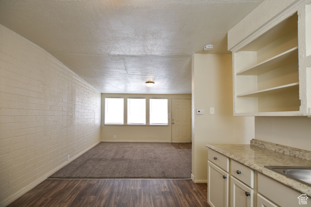 Interior space featuring brick wall, open shelves, light countertops, baseboards, and dark wood-style floors