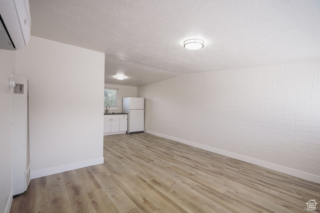 Unfurnished room featuring light wood-style floors, an AC wall unit, a heating unit, a textured ceiling, and baseboards
