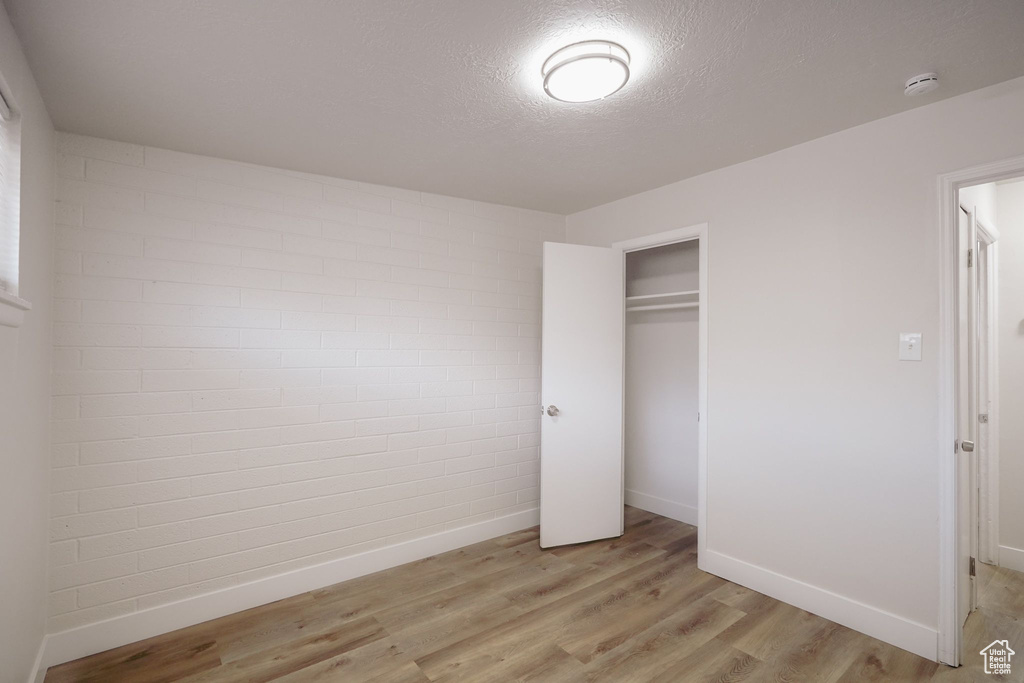 Unfurnished bedroom featuring baseboards, a textured ceiling, light wood-style flooring, and a closet