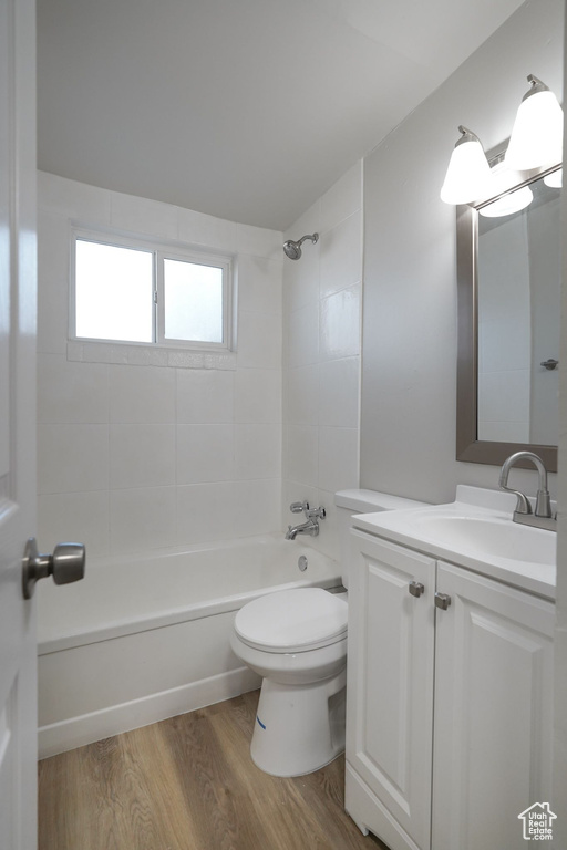 Bathroom with vanity, washtub / shower combination, wood finished floors, and toilet