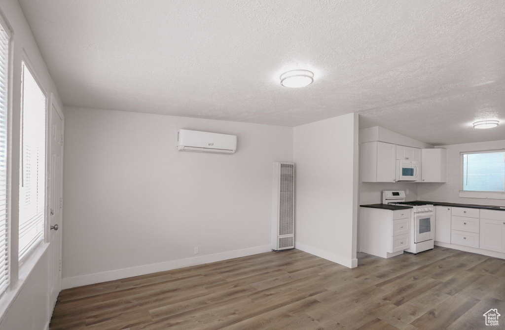 Kitchen with light wood-type flooring, a wall unit AC, white appliances, and a heating unit