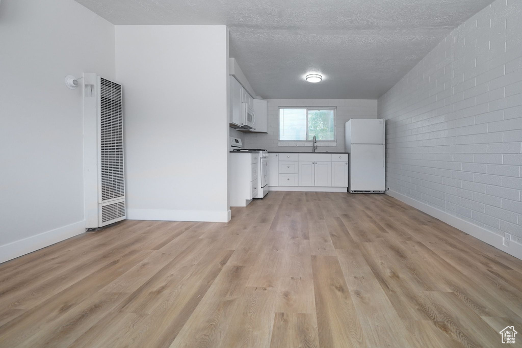 Interior space with a heating unit, brick wall, dark countertops, white appliances, and light wood-type flooring