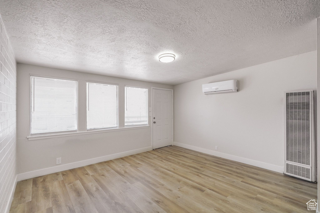 Empty room featuring light wood-style floors, a wall mounted AC, a textured ceiling, and a heating unit