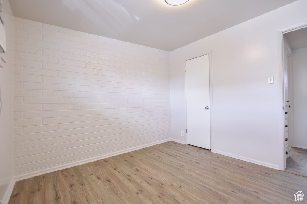 Unfurnished room featuring baseboards, light wood finished floors, and brick wall
