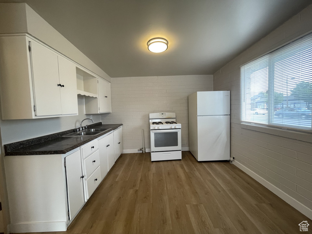 Kitchen featuring dark countertops, open shelves, wood finished floors, a sink, and white appliances