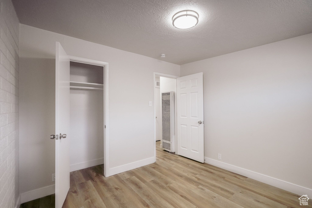 Unfurnished bedroom featuring a textured ceiling, baseboards, a closet, light wood-style flooring, and a heating unit