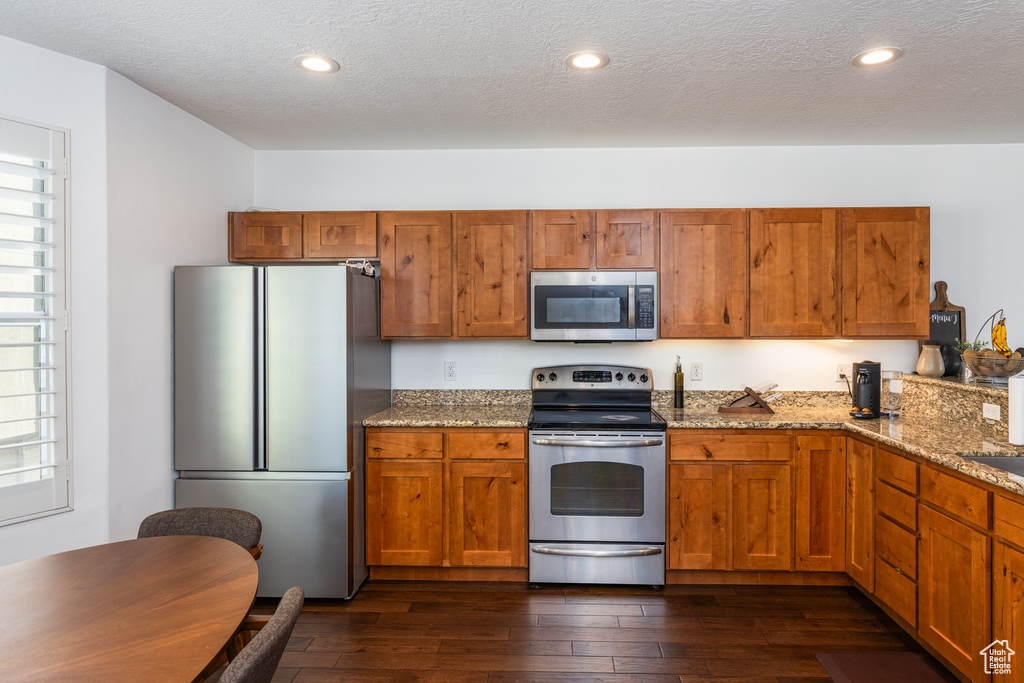 Kitchen with appliances with stainless steel finishes, a textured ceiling, light stone countertops, and dark wood-style floors
