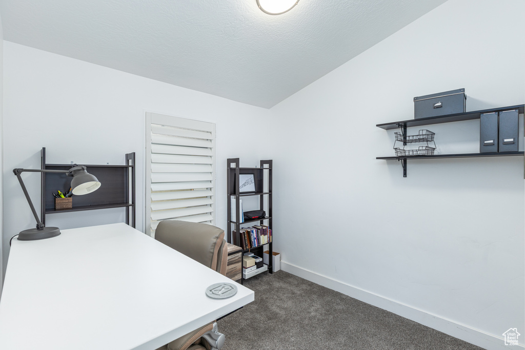 Office area featuring vaulted ceiling, dark colored carpet, and baseboards