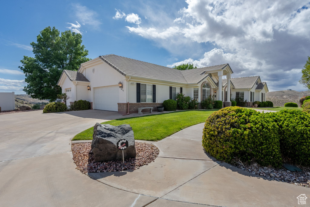 Ranch-style home with a tiled roof, a front yard, concrete driveway, an attached garage, and stucco siding
