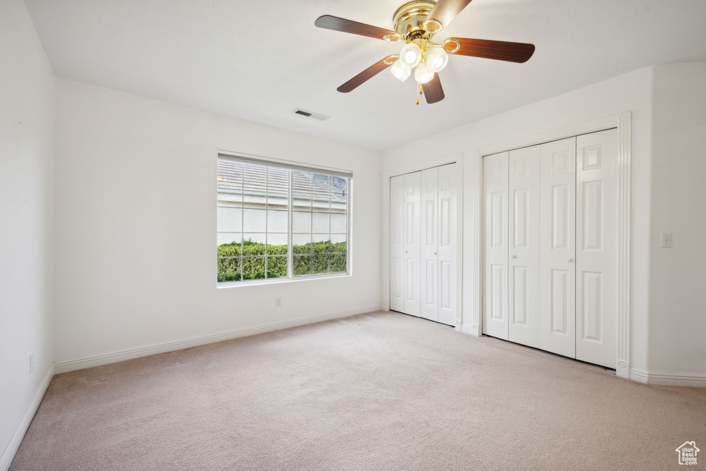 Unfurnished bedroom with visible vents, multiple closets, baseboards, and light carpet