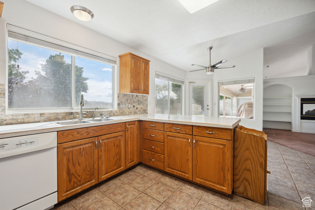 Kitchen with ceiling fan, a sink, dishwasher, light countertops, and a peninsula