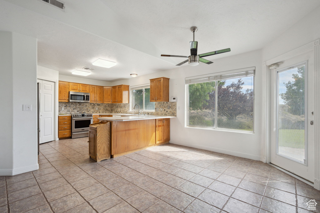 Kitchen with appliances with stainless steel finishes, light countertops, a peninsula, baseboards, and decorative backsplash
