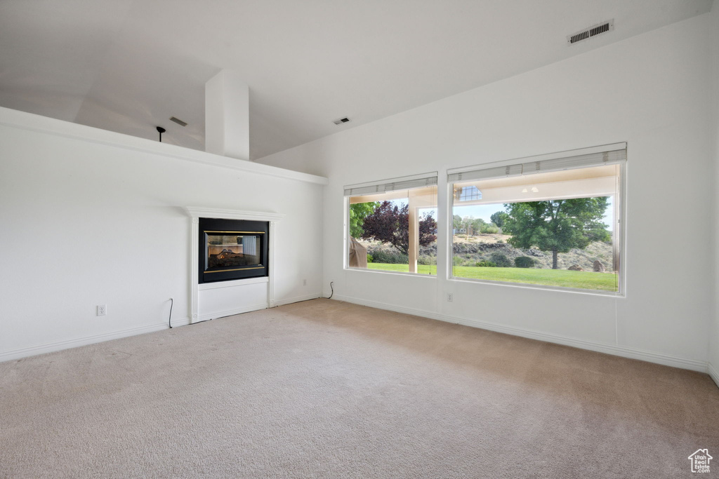 Unfurnished living room featuring visible vents, carpet flooring, a multi sided fireplace, and baseboards