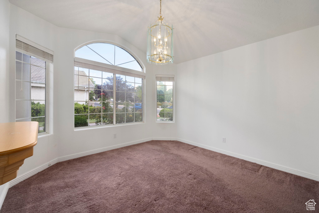 Carpeted empty room featuring an inviting chandelier, baseboards, and vaulted ceiling