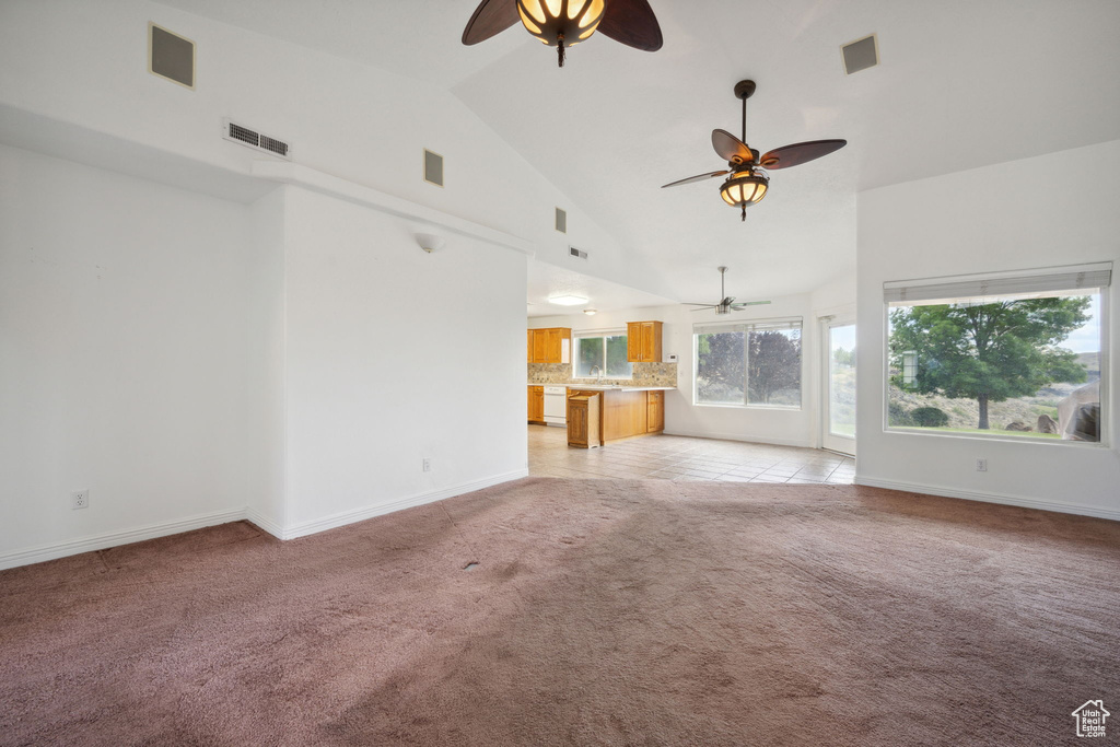 Unfurnished living room featuring ceiling fan, visible vents, high vaulted ceiling, baseboards, and light carpet