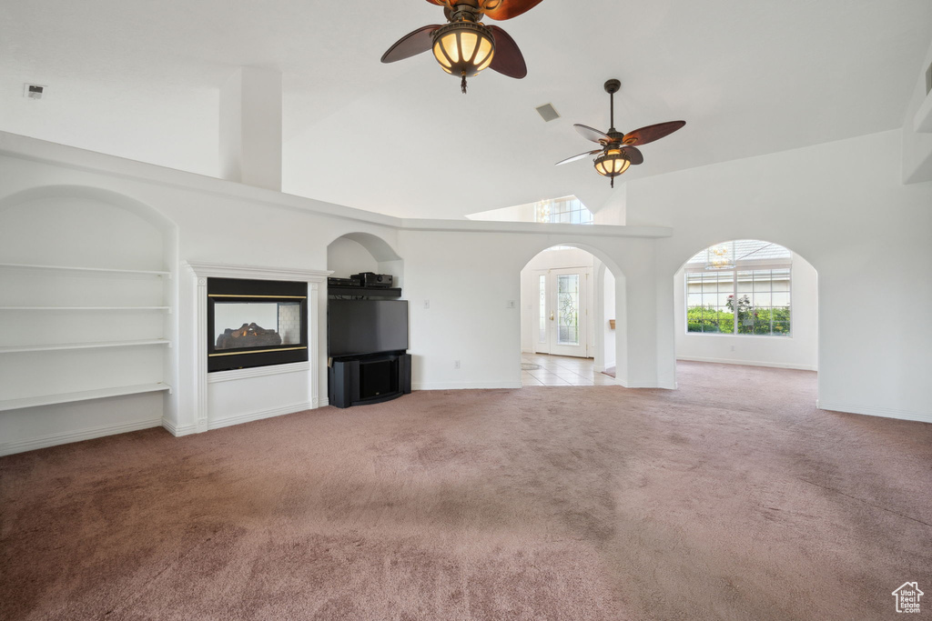 Unfurnished living room featuring high vaulted ceiling, light carpet, a ceiling fan, and arched walkways