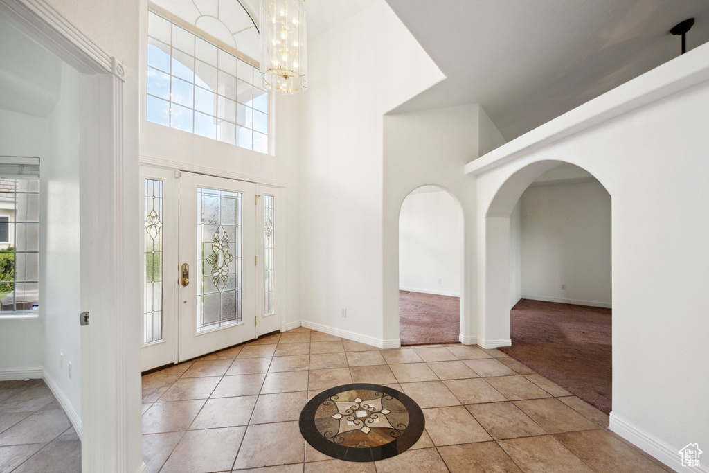 Tiled entrance foyer featuring arched walkways, a high ceiling, a notable chandelier, and baseboards