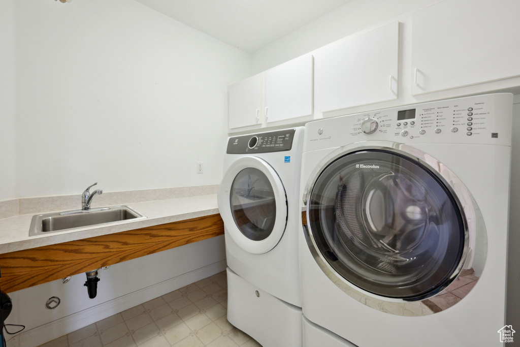 Clothes washing area with washer and dryer, light floors, a sink, and cabinet space